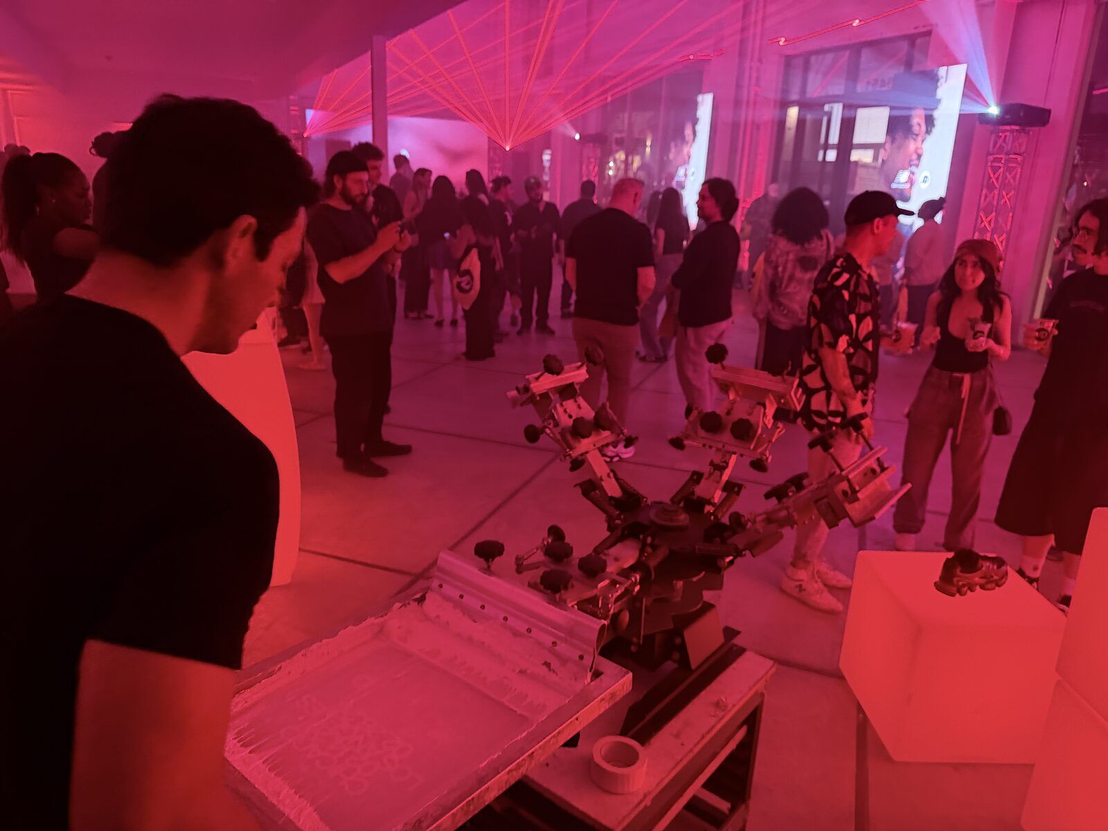Crew member preparing a live station while a launch afterparty crowd mingles under red lighting