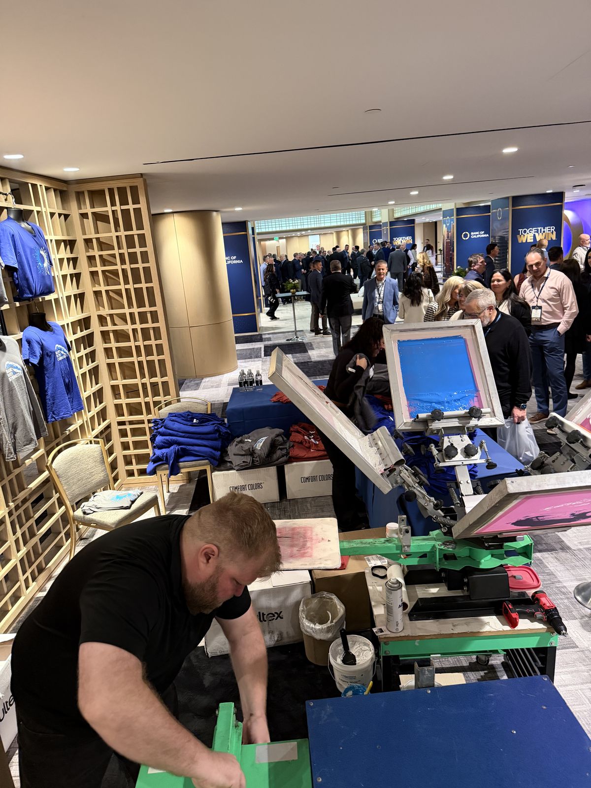 Attendees in business attire lining up at a merch station stocked with folded shirts at a banking conference
