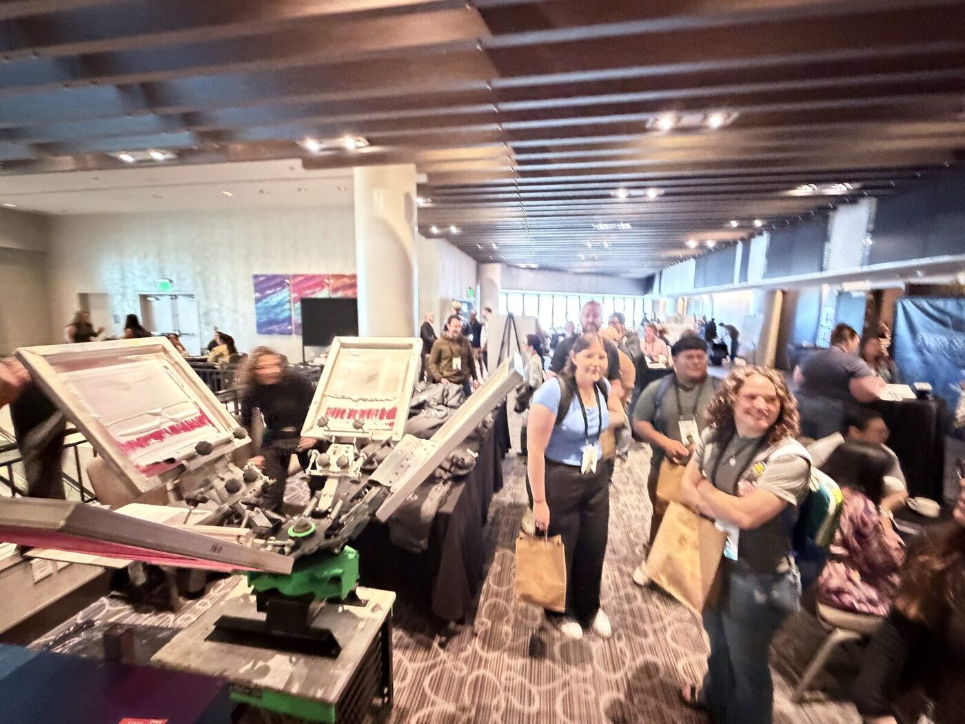 Conference guests smiling and carrying bags of freshly made custom merch through a hotel corridor